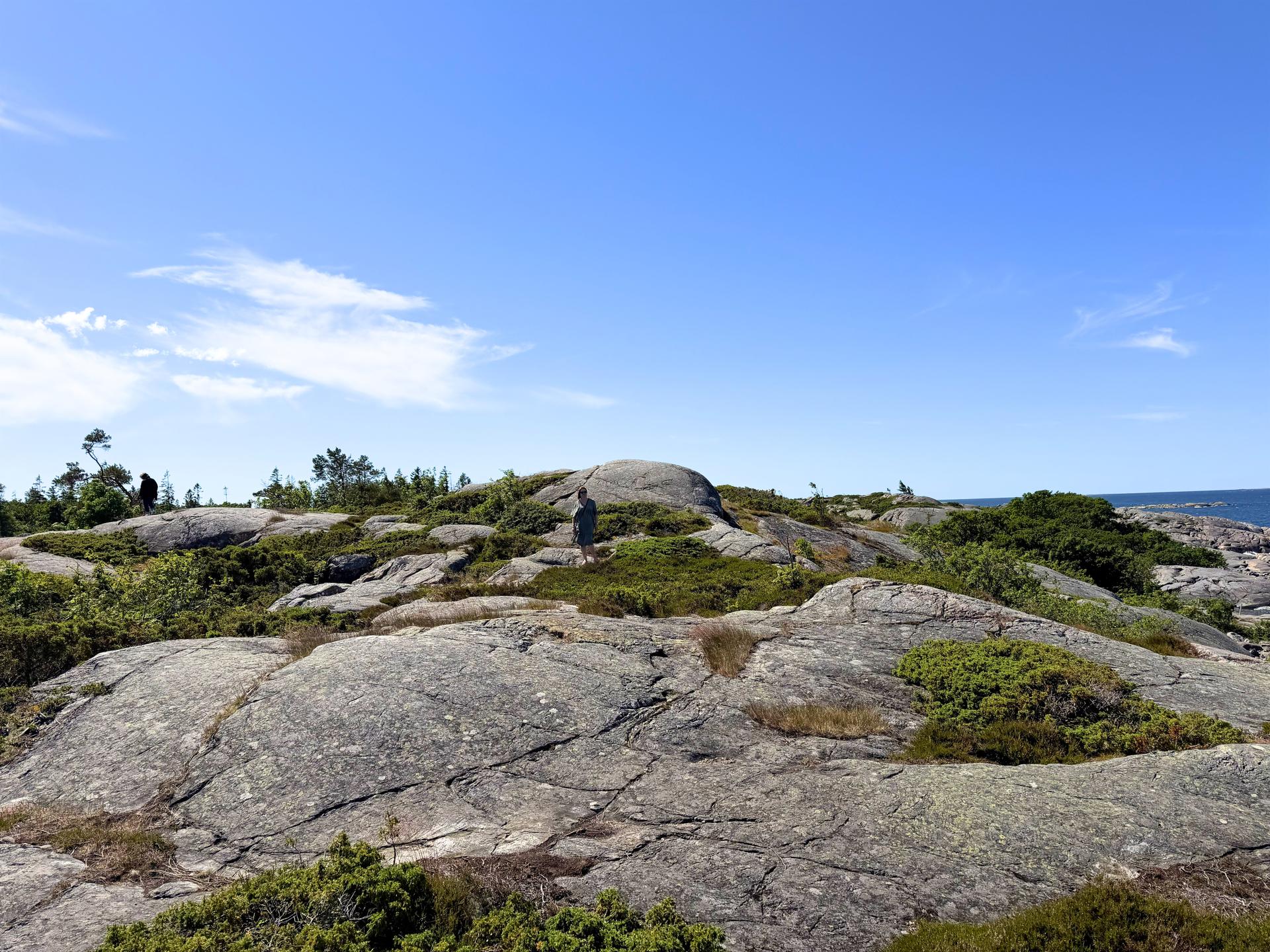 Kaksi ihmistä kulkee kallioisessa saaristomaisemassa.